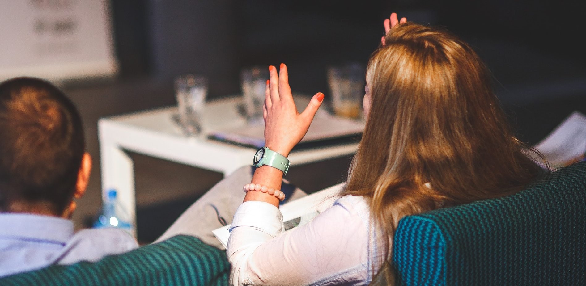 Back of a woman's head with her hands in the air as she explains something to others in the room