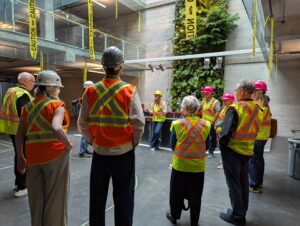 Group of donors in yellow vests and hard hat at a building renovation site. There is a natural wall as the backdrop.